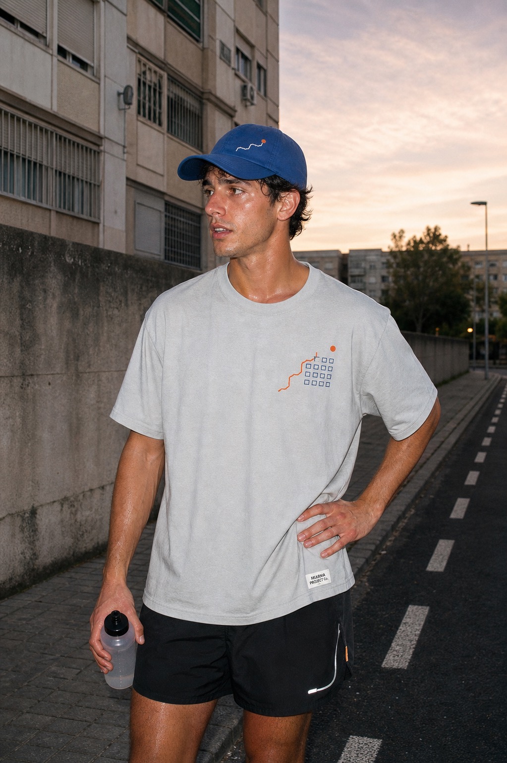 Adult runner wearing the ice-gray 3000 Viviendas Running Club tee and cobalt cap on a residential street at dawn.